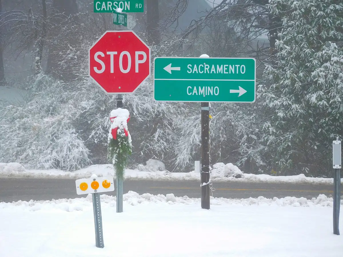 Snow covered intersection of Carson Road and Pony Express Trail with a highway sign pointing toward Camino