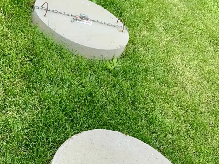 Chained concrete septic tank lids sitting at grade in a green lawn