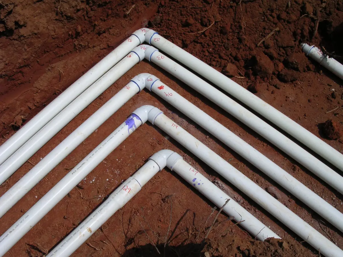 New white septic pipes laid in trenches of red soil before backfill