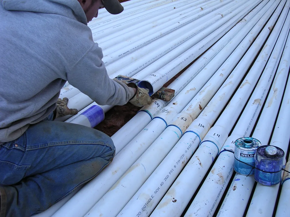 A gloved worker joins white plastic septic pipe with solvent cement during system work