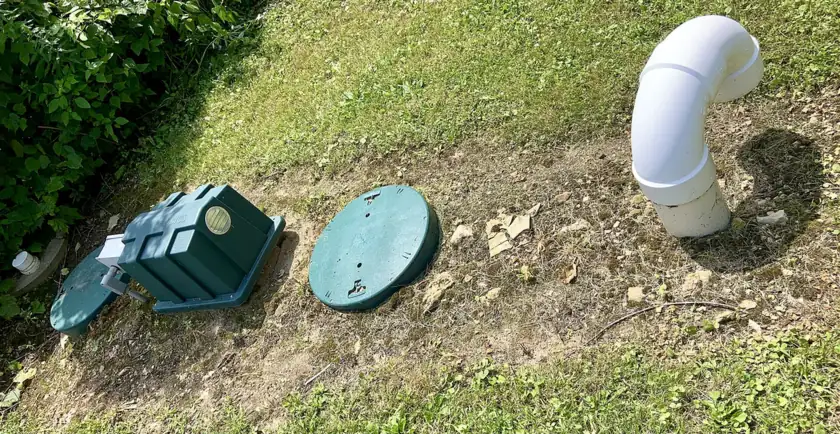 Green septic tank risers and lids finished at grade in a mowed lawn beside a vent pipe