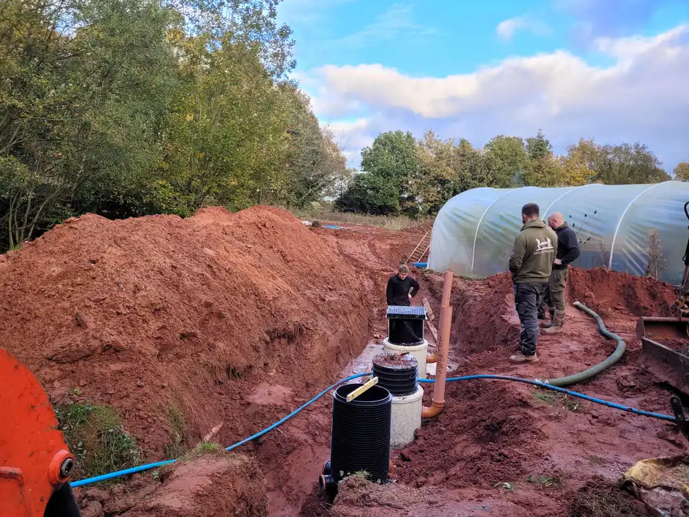 A crew sets a new septic tank with risers and plumbing in an open excavation