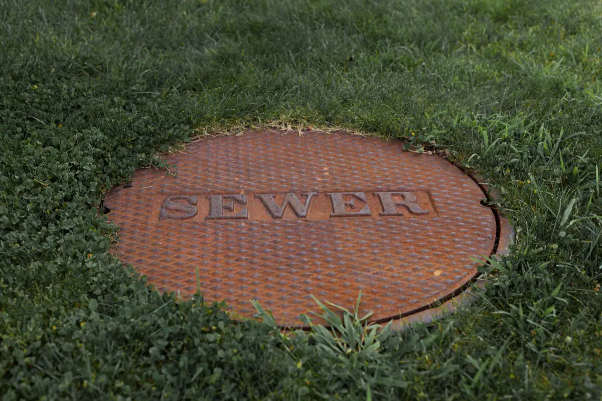 Rusted cast iron access lid set flush in a green lawn, the kind of buried lid a pump crew locates and exposes before service